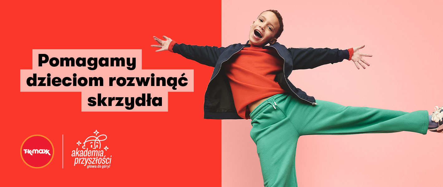 Uśmiechnięty chłopiec stoi z lewą nogą wyciągniętą do przodu.